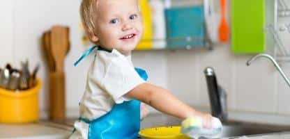 Filho de criança lavando pratos na cozinha. Garotinho se divertindo com a ajudar a sua mãe com o trabalho doméstico Filho de criança lavando pratos na cozinha. Garotinho se divertindo com a ajudar a sua mãe com o trabalho doméstico