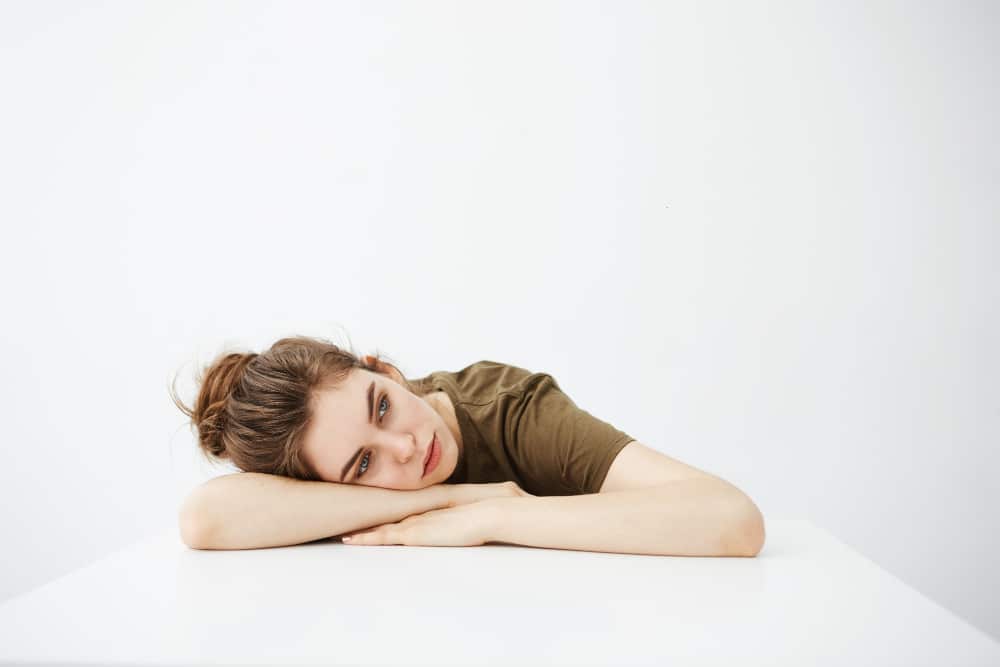 jovem mulher cansada que senta-se com a cabeça sobre a mesa com o fundo branco